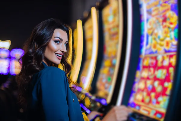 A woman smiling by bright slot machines showing lucky symbols, showcasing the exciting slot offerings at K55GAME.